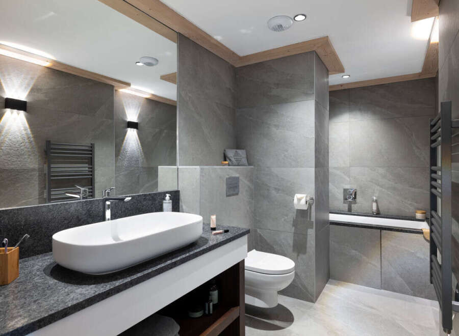 This luxurious bathroom boasts a modern design with sleek gray tiles, a spacious vanity with granite countertop, and a contemporary oval sink.