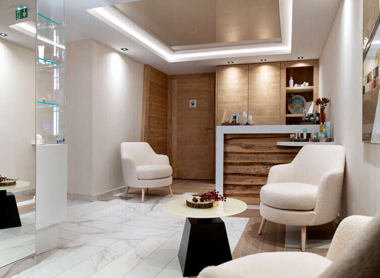 Relax in our luxurious spa waiting area, featuring plush armchairs, modern artwork, and a sleek reception desk.