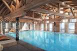Indulge in luxury at this stunning chalet featuring a spacious indoor pool, surrounded by wooden beams and large windows offering breathtaking views.