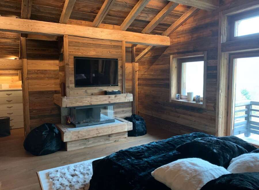 This stunning chalet boasts a rustic-chic bedroom with exposed wooden beams, a cozy fireplace, and plush furnishings.