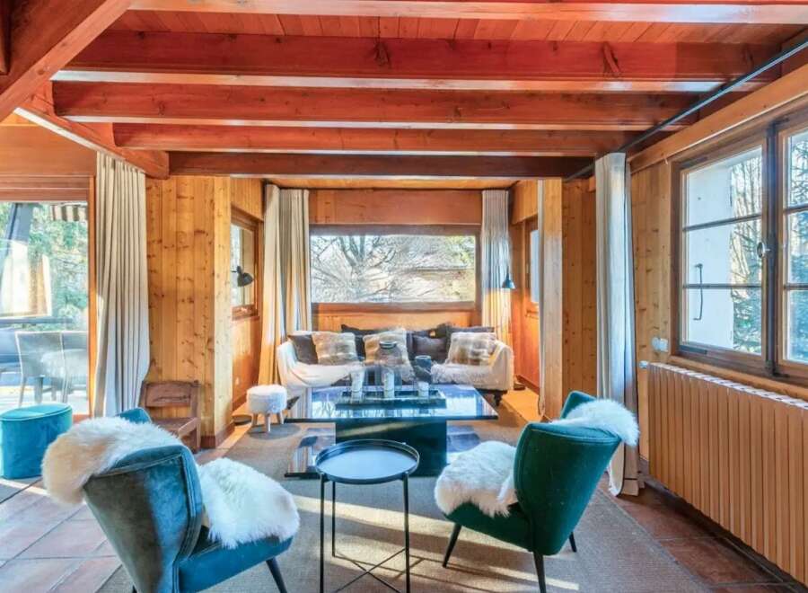 Cozy chalet living room with wood-beamed ceilings, large windows offering scenic views, and comfortable seating arrangements.