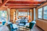 Cozy chalet living room with wood-beamed ceilings, large windows offering scenic views, and comfortable seating arrangements.