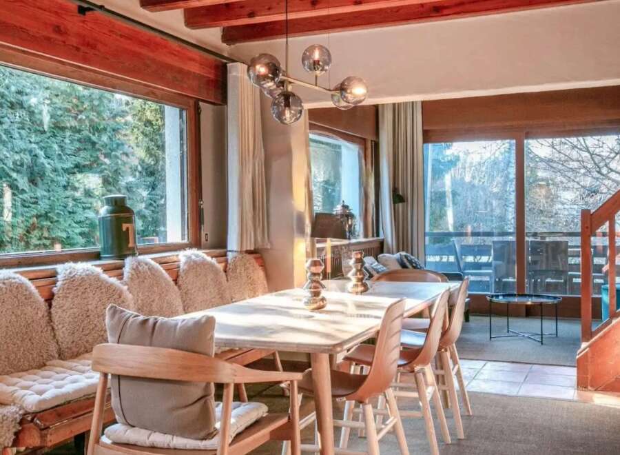 This stunning chalet boasts a spacious dining area with a large table perfect for family gatherings, bathed in natural light from expansive windows showcasing breathtaking views.