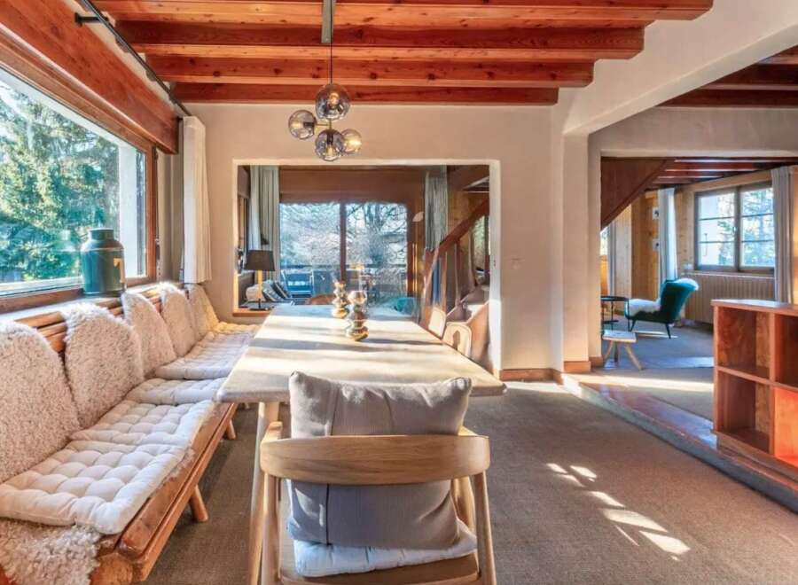 This stunning chalet boasts a spacious dining area with a long wooden table perfect for gatherings, complemented by comfortable built-in seating with sheepskin throws.
