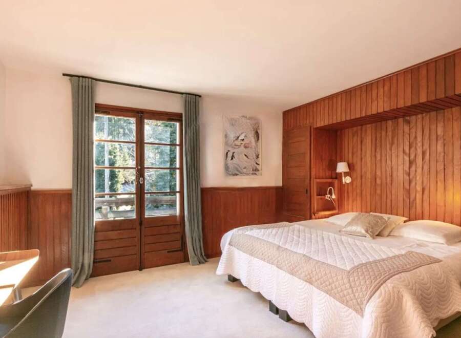 This stunning bedroom boasts a king-size bed with a luxurious quilt, complemented by wood paneling and large windows offering scenic views.
