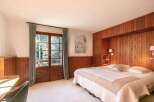 This stunning bedroom boasts a king-size bed with a luxurious quilt, complemented by wood paneling and large windows offering scenic views.