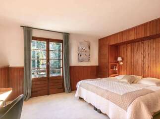 This stunning bedroom boasts a king-size bed with a luxurious quilt, complemented by wood paneling and large windows offering scenic views.