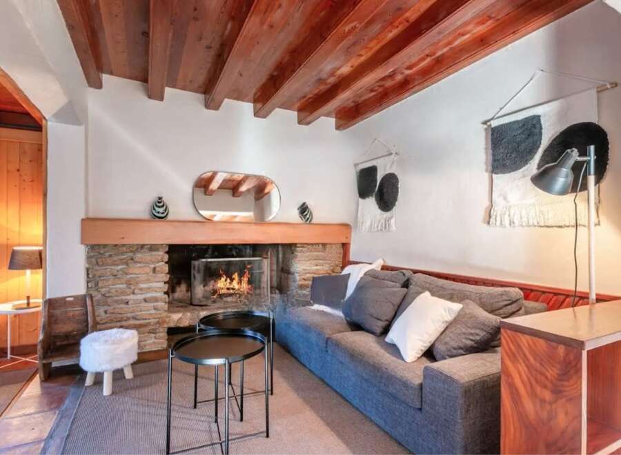 Cozy living room with a stone fireplace, wooden beams, and comfortable gray sofa.