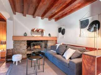 Cozy living room with a stone fireplace, wooden beams, and comfortable gray sofa.