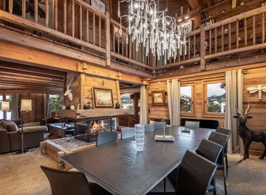 This luxurious chalet boasts a stunning open-plan living area with a large dining table perfect for gatherings, a cozy fireplace, and high ceilings.