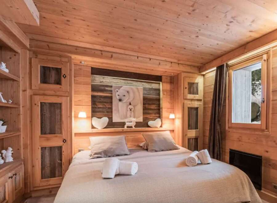 Cozy chalet bedroom with wooden walls and ceiling, featuring a comfortable double bed and built-in wooden wardrobe.