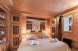 Cozy chalet bedroom with wooden walls and ceiling, featuring a comfortable double bed and built-in wooden wardrobe.