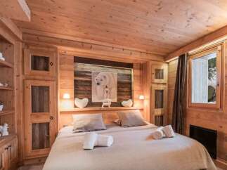 Cozy chalet bedroom with wooden walls and ceiling, featuring a comfortable double bed and built-in wooden wardrobe.