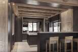 This stunning kitchen boasts a dark wood and grey stone bar, a central island, and exposed beam ceiling.