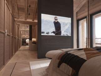 Luxury chalet bedroom with stunning mountain views and a built-in TV showcasing a James Bond movie.