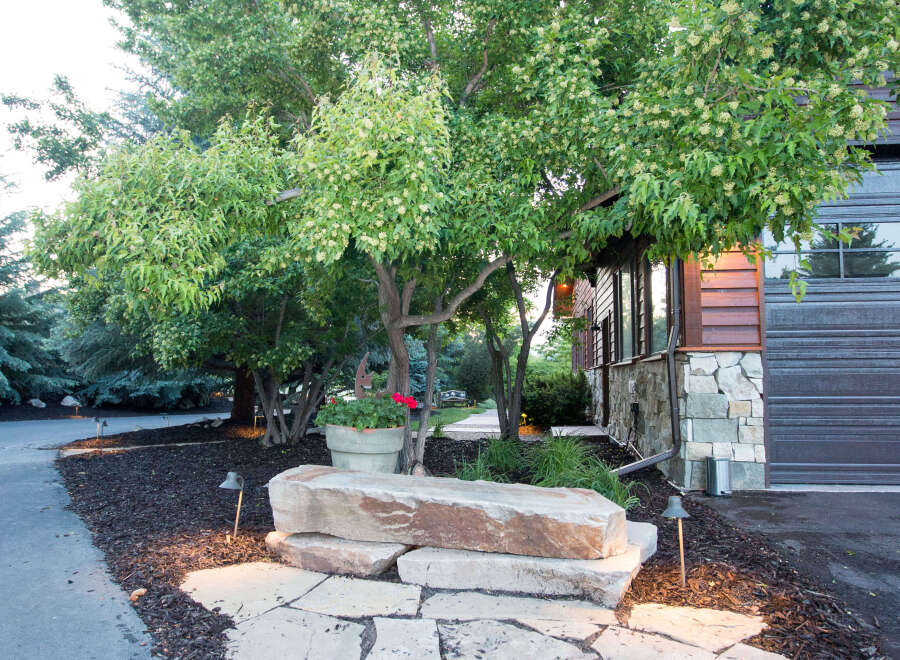 This stunning property boasts a beautifully landscaped front yard, featuring a natural stone pathway leading to a unique rock bench.
