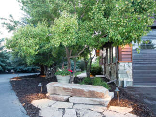 This stunning property boasts a beautifully landscaped front yard, featuring a natural stone pathway leading to a unique rock bench.