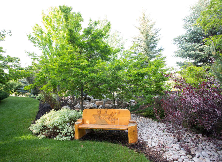 Discover the tranquility of this beautifully landscaped property, featuring a charming wooden bench perfect for relaxing.