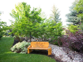 Discover the tranquility of this beautifully landscaped property, featuring a charming wooden bench perfect for relaxing.
