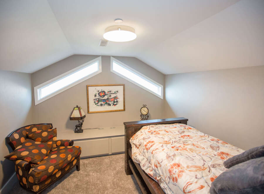 This cozy bedroom features a unique design with angled ceilings and natural light from the windows.