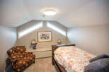 This cozy bedroom features a unique design with angled ceilings and natural light from the windows.