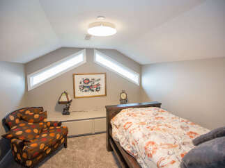 This cozy bedroom features a unique design with angled ceilings and natural light from the windows.
