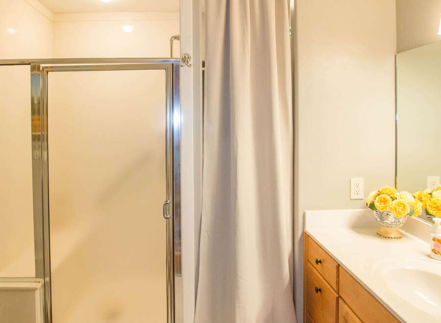 This bathroom features a modern shower with a glass door and a neutral-toned curtain for privacy.