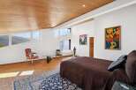 This luxurious bedroom boasts stunning mountain views through its uniquely shaped windows, complemented by a wooden ceiling and hardwood floors.