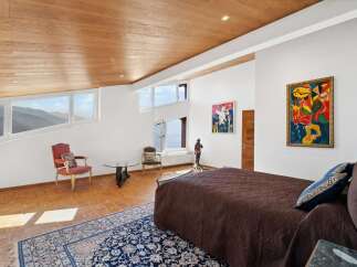 This luxurious bedroom boasts stunning mountain views through its uniquely shaped windows, complemented by a wooden ceiling and hardwood floors.