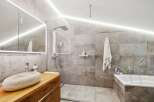 Modern bathroom with a walk-in shower, bathtub, and stylish stone sink.