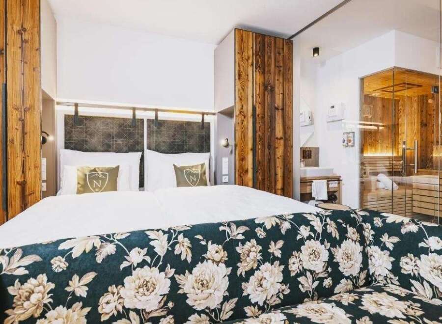 Experience luxury in this stunning hotel room, featuring a cozy bed and a beautifully designed floral sofa.