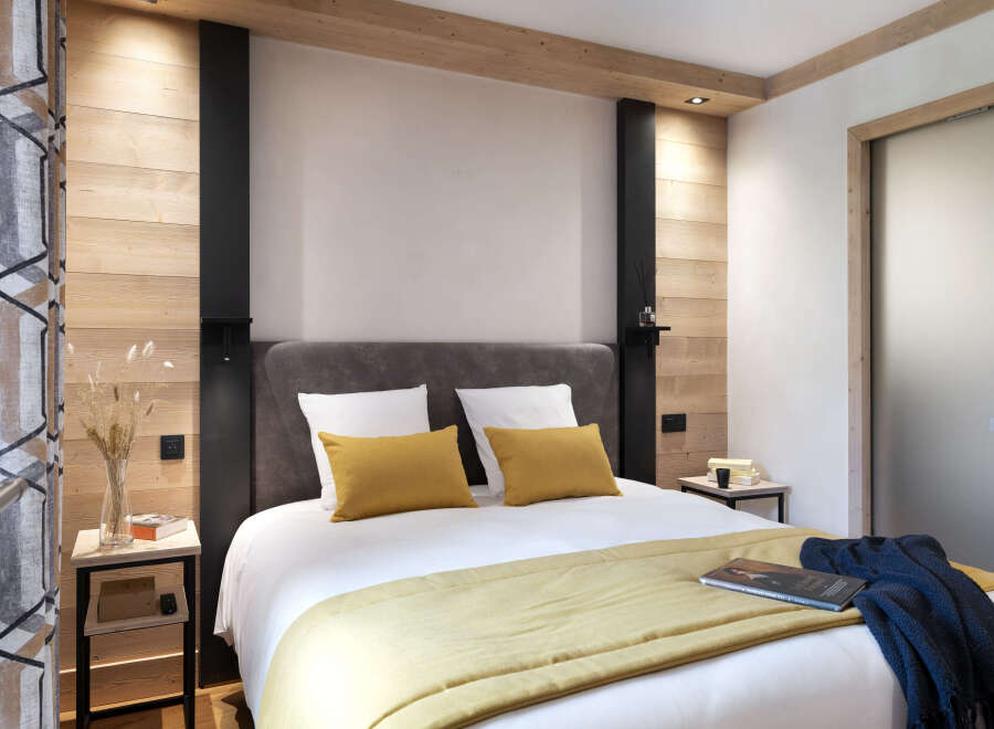 This cozy bedroom features a comfortable double bed with a mustard yellow throw, complemented by a dark blue knitted blanket.
