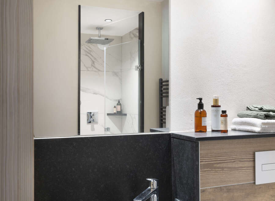This modern bathroom boasts a sleek, dark-colored sink and a spacious walk-in shower with marble tile.