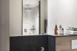 This modern bathroom boasts a sleek, dark-colored sink and a spacious walk-in shower with marble tile.