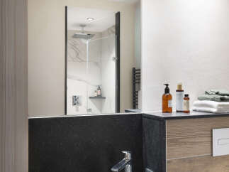 This modern bathroom boasts a sleek, dark-colored sink and a spacious walk-in shower with marble tile.