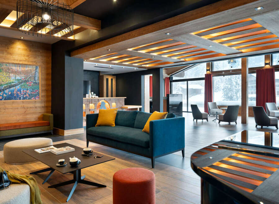 This stunning hotel lobby boasts a cozy and sophisticated atmosphere, featuring a teal sofa with yellow throw pillows, a modern coffee table, and a sleek black piano.