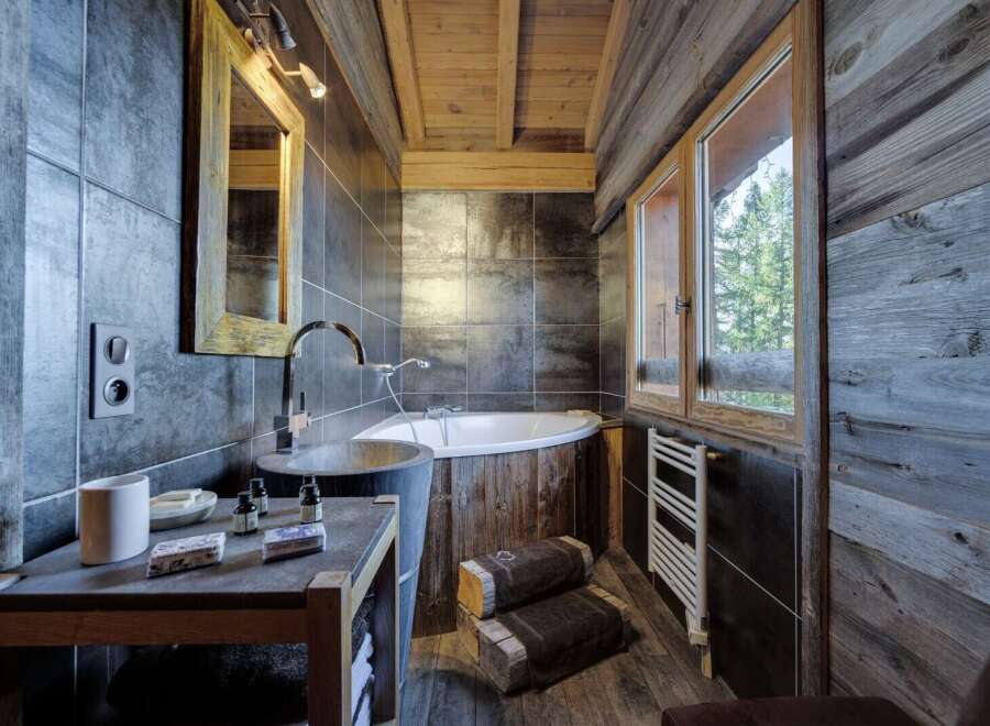 This luxurious bathroom boasts a rustic-chic design with dark gray tiles, reclaimed wood accents, and a stunning freestanding bathtub.