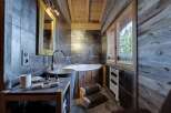 This luxurious bathroom boasts a rustic-chic design with dark gray tiles, reclaimed wood accents, and a stunning freestanding bathtub.