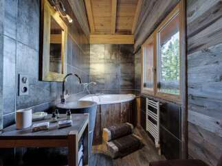 This luxurious bathroom boasts a rustic-chic design with dark gray tiles, reclaimed wood accents, and a stunning freestanding bathtub.