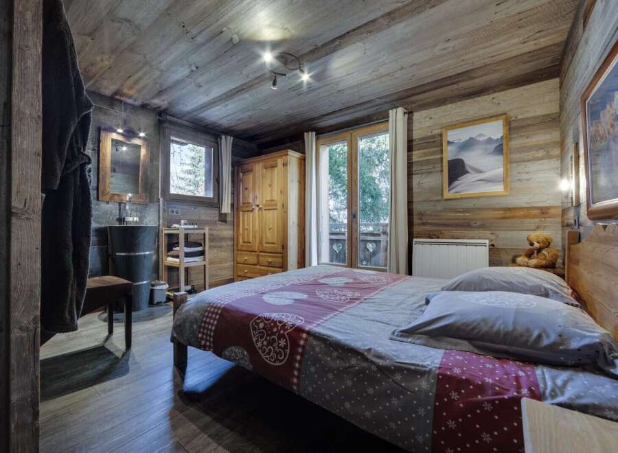 Cozy chalet bedroom with rustic wood walls and floors, featuring a comfortable double bed and a private bathroom.