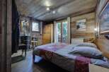 Cozy chalet bedroom with rustic wood walls and floors, featuring a comfortable double bed and a private bathroom.