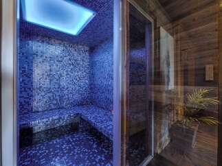 Indulge in ultimate relaxation in this stunning private steam room, featuring a sleek blue mosaic design and a calming blue light.