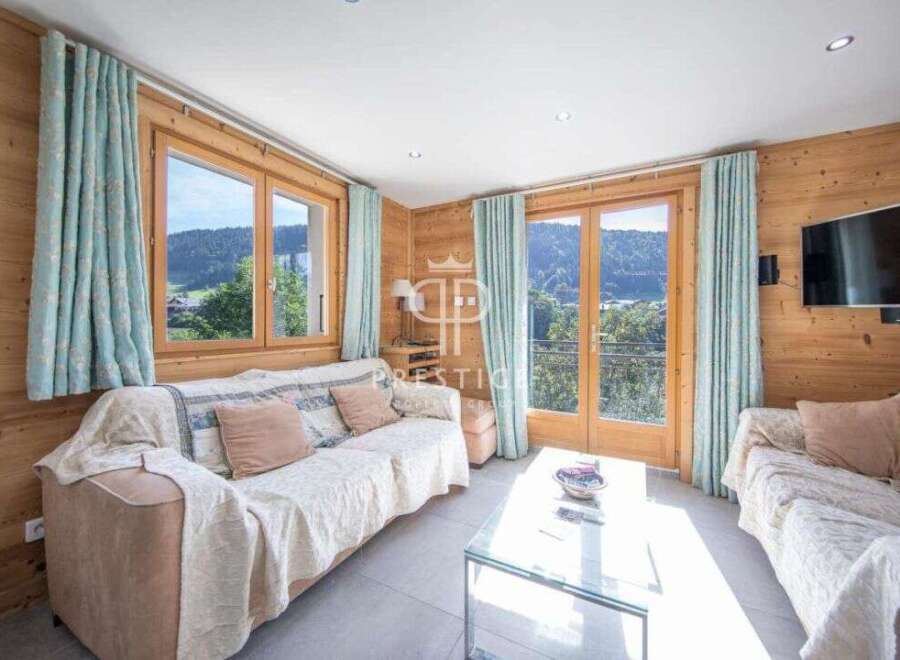 Experience the charm of this cozy living room, featuring stunning wooden walls and large windows that frame breathtaking mountain views.
