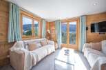 Experience the charm of this cozy living room, featuring stunning wooden walls and large windows that frame breathtaking mountain views.
