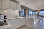 Modern kitchen with marble countertops and white cabinets, open to a dining area with large windows offering scenic views.