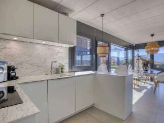 Modern kitchen with marble countertops and white cabinets, open to a dining area with large windows offering scenic views.