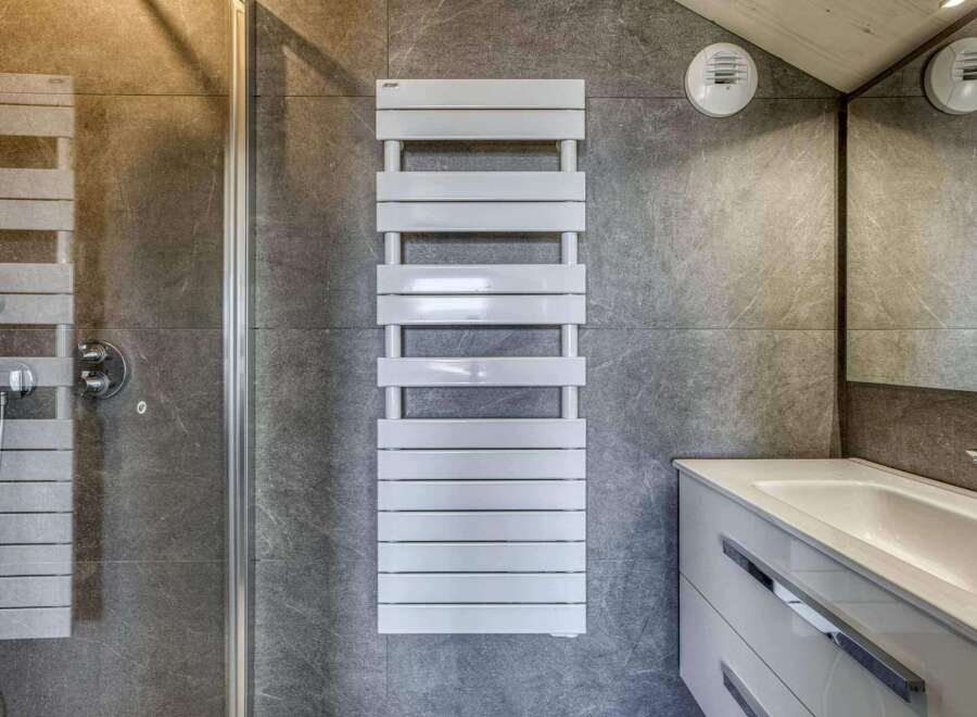 Modern bathroom with sleek gray tile, a frameless glass shower enclosure, and a contemporary white heated towel rack.