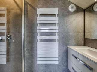 Modern bathroom with sleek gray tile, a frameless glass shower enclosure, and a contemporary white heated towel rack.