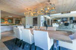 This stunning chalet boasts a spacious dining area with a rustic wooden table and modern white chairs, illuminated by a unique circular chandelier.