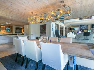 This stunning chalet boasts a spacious dining area with a rustic wooden table and modern white chairs, illuminated by a unique circular chandelier.